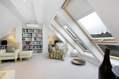 an attic living room with white walls and flooring, bookshelves in the corner