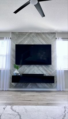 a living room with a flat screen tv on the wall and a ceiling fan in front of it