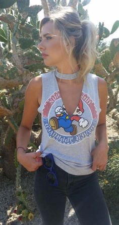 a woman wearing a tank top with an angry bird on the front and back, standing next to a pine tree