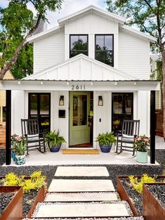 a white house with two rocking chairs on the front porch and potted plants outside