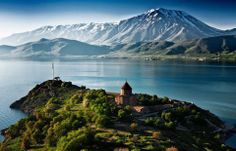 an island with a church on it in the middle of water and mountains behind it