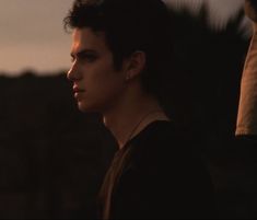 a man with dark hair and piercings standing in front of the sun at dusk