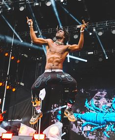 a shirtless man performing on stage with his hands in the air