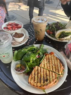 there is a sandwich and salad on the table with cups of coffee next to it