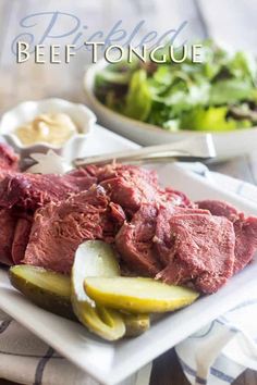 a white plate topped with meat and pickles next to a bowl of lettuce