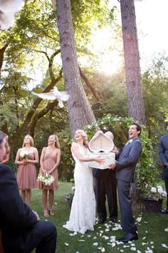 a bride and groom holding an umbrella in front of their wedding party at the park