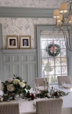 a dining room table is set with white flowers and greenery