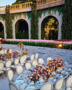 an outdoor dining area with tables, chairs and flowers on the table in front of a stone wall