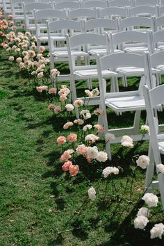 rows of white folding chairs with pink and white flowers on the grass in front of them