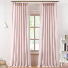 a pink curtain hanging in front of a window next to a book shelf and chair