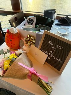 a table with flowers and cards on it near a window that says will you be my girlfriend?