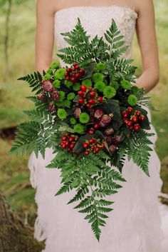 a bride holding a bouquet of red berries and green leaves on her wedding day in the woods