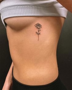 a woman's stomach with a single rose tattoo on her left side ribcage