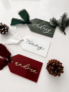 three tags with pine cones and evergreens on top of each tag, one has the word family written on it