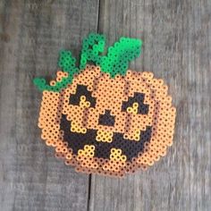 a perler bead pumpkin is sitting on a wooden surface, it looks like the face of a pumpkin