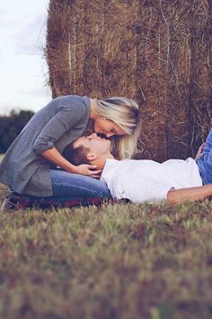 two people laying on the ground in front of hay bales with one person kissing the other