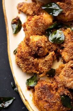 some fried food is on a white plate with green leafy greens and seasoning