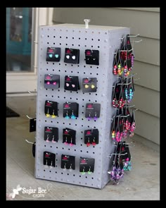 a rack with earrings hanging on it in front of a house and the door is open