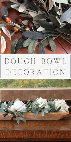 a bowl filled with white flowers and greenery on top of a wooden table next to a