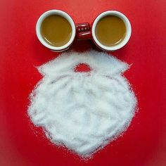 two cups of coffee sit next to each other on a red surface with white powder