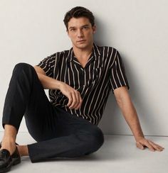 a man is sitting on the floor with his legs crossed and wearing black pants, striped shirt and loafers