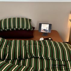 a bed with green and white striped comforter next to a lamp on a table