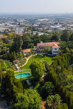 an aerial view of a large house surrounded by trees and houses in the distance with a swimming pool