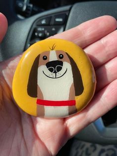 a hand holding a yellow and brown dog pin with a red collar on it's head