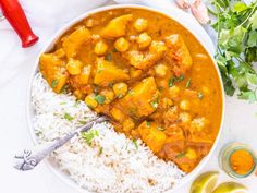 a white bowl filled with rice and curry next to some cilantro sauce on the side