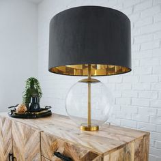 a table with a lamp on top of it next to a brick wall and a potted plant