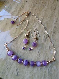 "These amethyst faceted rounds are beautiful, each one hand crafted and unique. I used antique gold plated pewter hex rondelles to separate them. The smooth rounds are gold fill, as well as the paperclip chain, wire guards and lobster claw clasp. The necklace is adjustable at 18\", 19\" and 20\". I added small amethyst cubes to the drop earrings and antique gold plated lotus flowers. The flat fishhook ear wires with ball and coil are also gold fill. They drop 2 1/4\".  *Amethyst facet rounds, cubes & flat oval *Antique gold plate hex rondelles & lotus flowers (pewter) *Gold fill smooth rounds, paperclip chain, wire guards, lobster claw & flat fishhook ear wires *Gold plate rings & pins *Adjustable necklace - 18\", 19\" & 20\" *Earring - 2 1/4\"H" Gold Rondelle Bohemian Jewelry, Bohemian Gold Rondelle Jewelry, Faceted Round Brass Jewelry, Gold Rondelle Jewelry With Faceted Beads, Gold Faceted Brass Jewelry, Faceted Gold Brass Jewelry, Adjustable Faceted Amethyst Jewelry, Lavender Round Jewelry With Faceted Beads, Gold Brass Jewelry With Faceted Beads