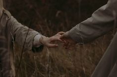 two people holding hands while walking through tall grass