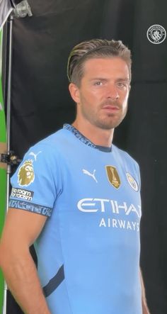 a man standing in front of a green wall wearing a blue shirt and black shorts