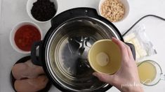 a person is holding a cup in front of an electric blender filled with ingredients