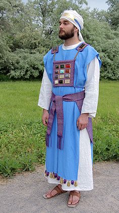 a man wearing a blue and white outfit standing in front of some green grass with trees behind him