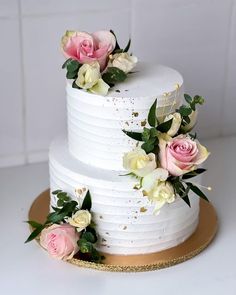 a three tiered white cake with pink and white flowers on the top, sitting on a gold platter