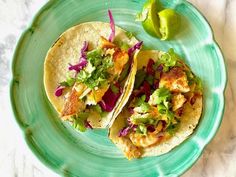 two fish tacos on a green plate next to a lime and some red cabbage