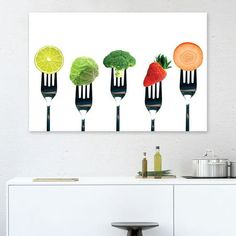 forks with different fruits and vegetables on them are hanging above a white cabinet in a kitchen