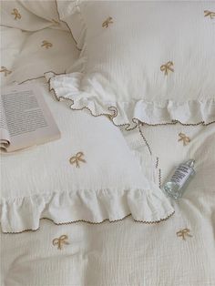 an open book is laying on a bed with white sheets and ruffled edges, next to a bottle of water