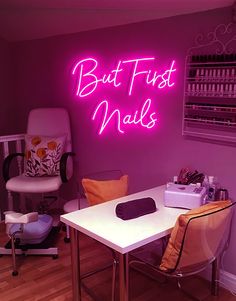 a pink neon sign that says but first nails on the wall above a white table