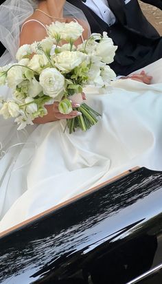 a bride and groom are sitting in the back of a black car with white flowers