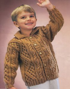 a young boy wearing a brown sweater and white pants with his hand in the air