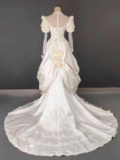 a white wedding dress with long sleeves and flowers on the skirt is sitting on a mannequin