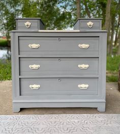 a grey dresser with gold handles and knobs on it's drawers in front of some trees