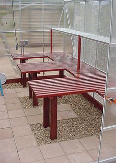 several wooden benches in a greenhouse with glass walls and gravel flooring on the ground