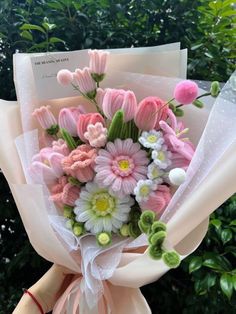 a bouquet of pink and white flowers is held by someone's hand in front of some bushes