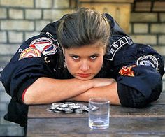 a woman leaning over a wooden table next to a glass filled with water and coins