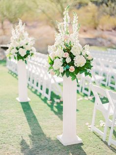 two tall white vases with flowers on them are sitting in front of rows of chairs