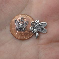 a tiny silver bee charm sitting on top of a penny coin in someone's hand