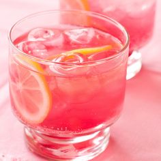 two glasses filled with drinks sitting on top of a pink table cloth covered tablecloth